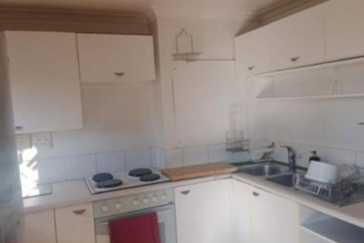 A compact kitchen featuring white built-in cabinetry, an electric hob, an oven, and a double sink with a tiled backsplash.