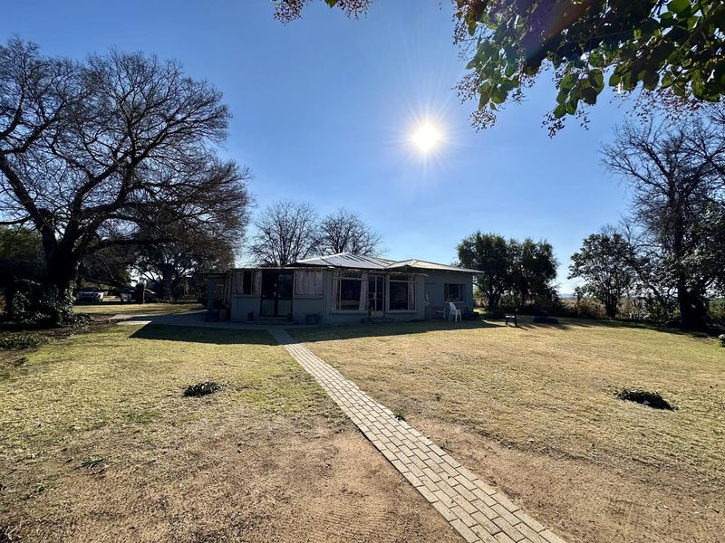 A rear view of the property featuring a paved walkway leading to the house, surrounded by a spacious garden and mature trees.
