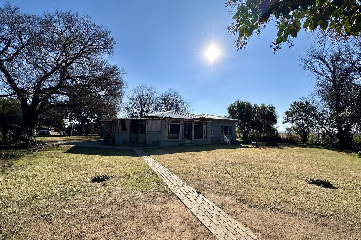 A rear view of the property featuring a paved walkway leading to the house, surrounded by a spacious garden and mature trees.