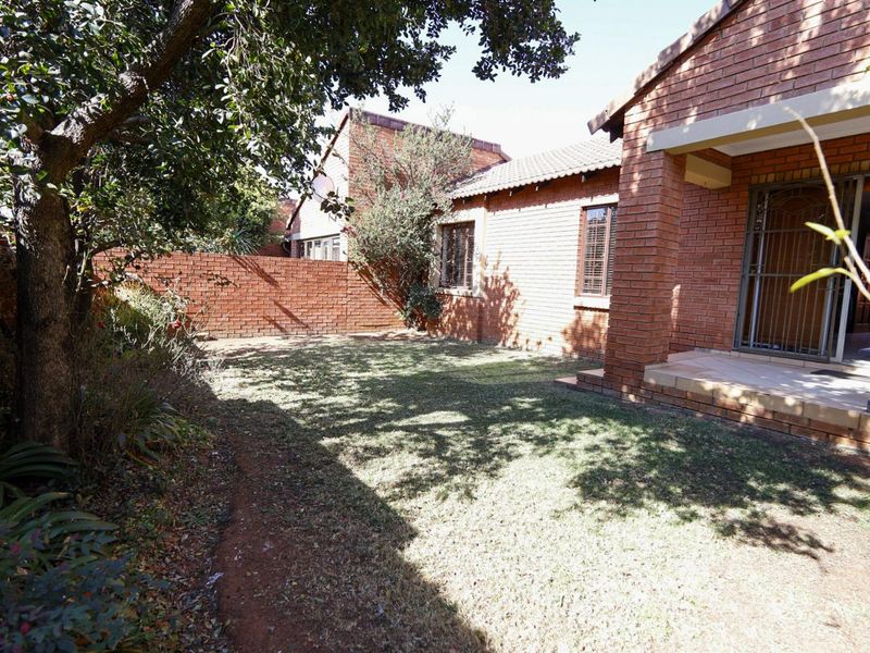 A private rear garden featuring a lawn, brick boundary walls, and a covered patio area with security gate access to the townhouse interior.