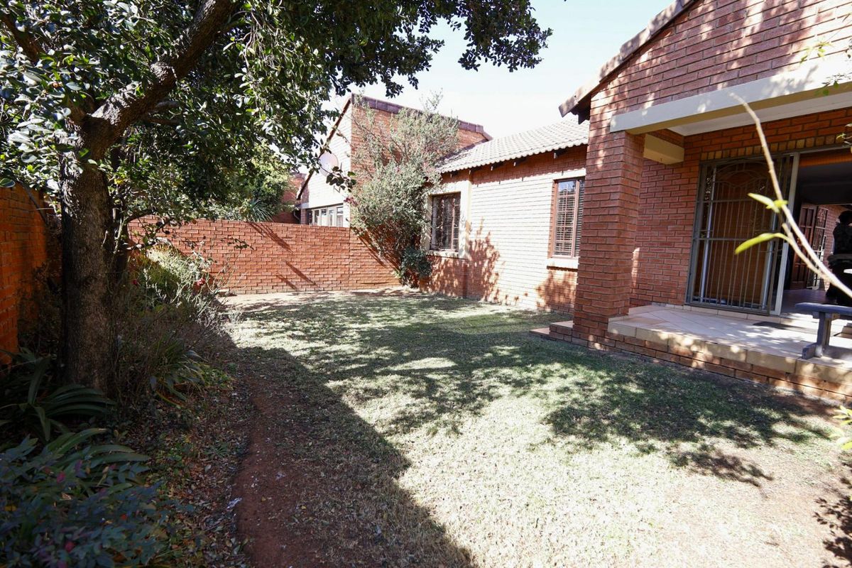 A private rear garden featuring a lawn, brick boundary walls, and a covered patio area with security gate access to the townhouse interior.