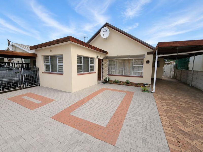 Front elevation of a single-story house featuring a paved driveway, carport, and secure gated entrance with well-maintained exterior finishes.