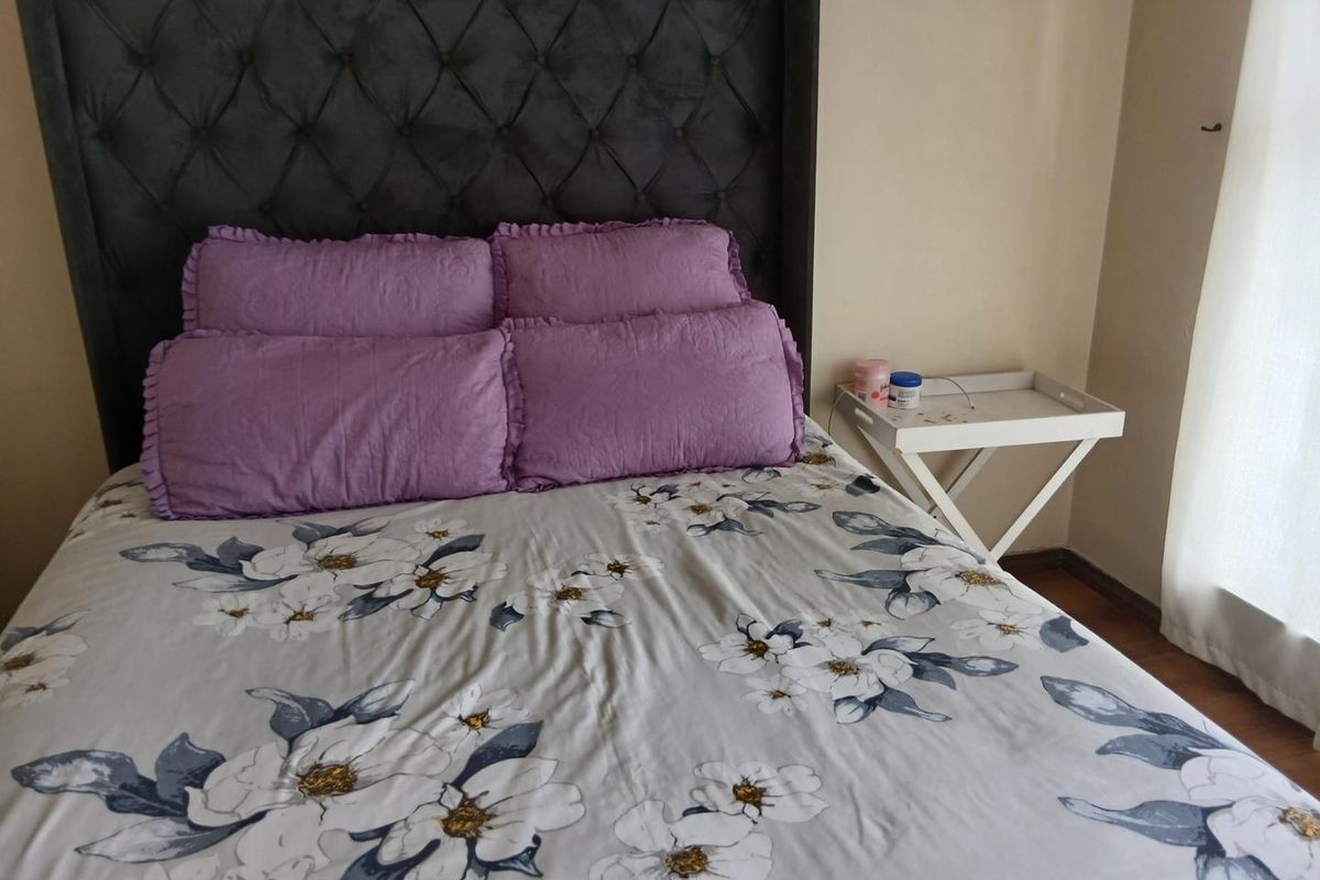 A cozy bedroom featuring a large dark grey tufted headboard and warm-toned laminate flooring.