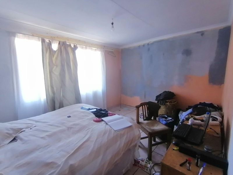 A bedroom featuring tiled flooring and a window with curtain rods, currently requiring wall finishing and painting to complete the space.