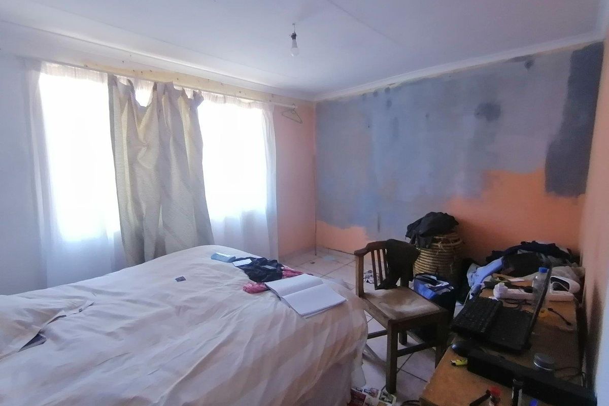 A bedroom featuring tiled flooring and a window with curtain rods, currently requiring wall finishing and painting to complete the space.