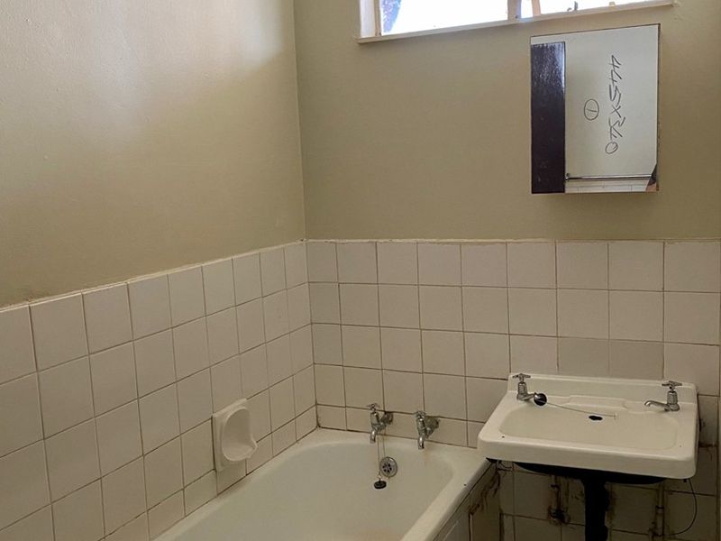 A dated bathroom featuring a standard bathtub, wall-mounted basin, and tiled splashback, requiring renovation to modernize the space.