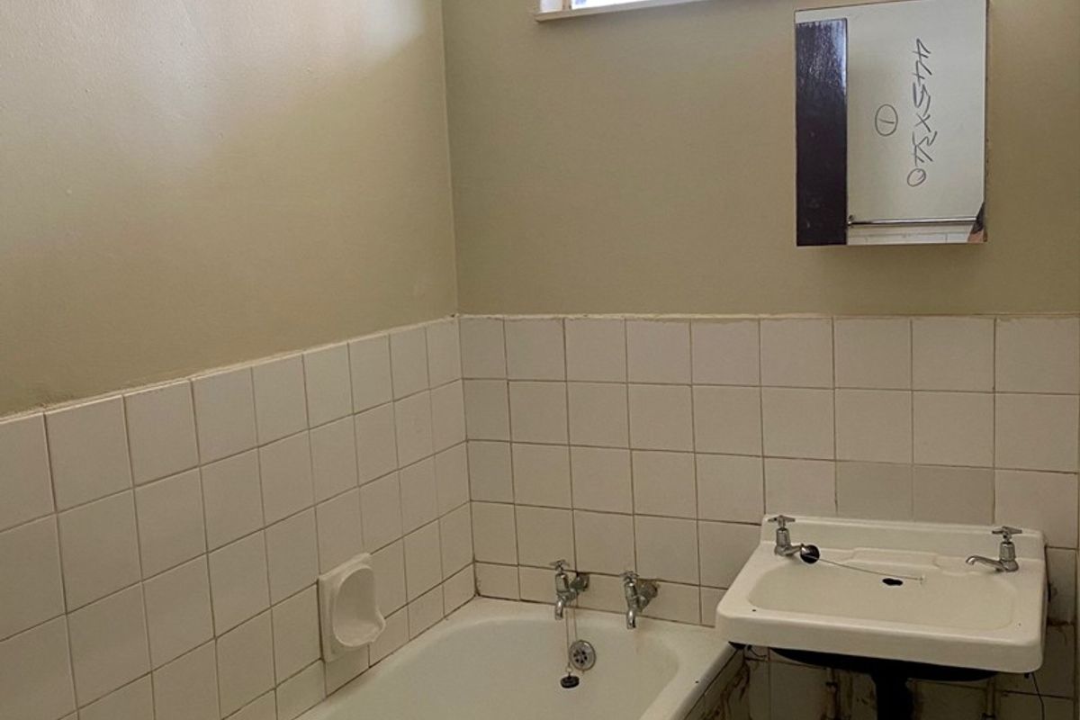 A dated bathroom featuring a standard bathtub, wall-mounted basin, and tiled splashback, requiring renovation to modernize the space.