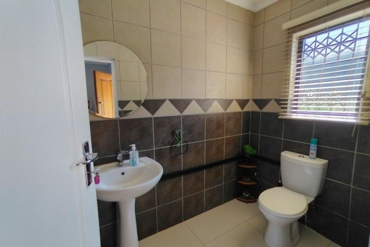 A functional bathroom featuring a pedestal basin, toilet, and two-tone tiled walls with decorative border accents and security bars on the window.