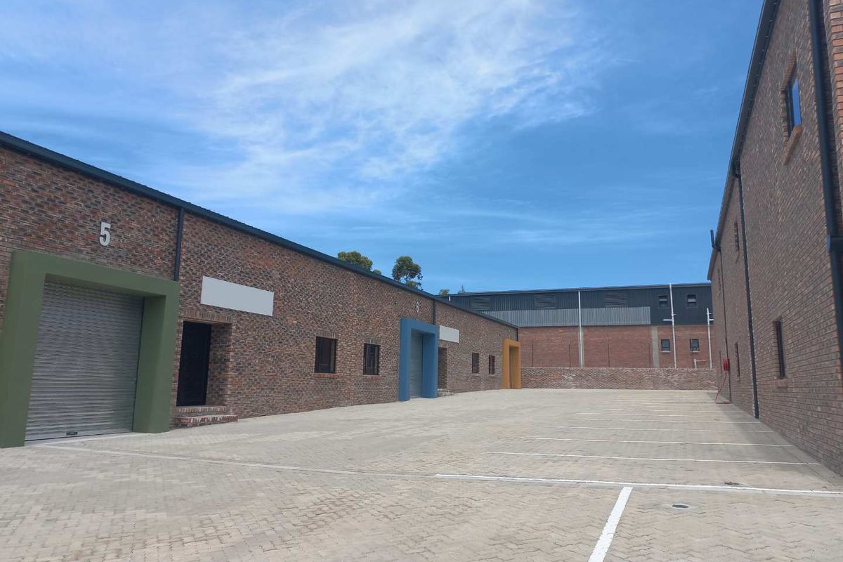 A view of the exterior courtyard and parking area featuring modern face-brick industrial units with roller shutter doors.