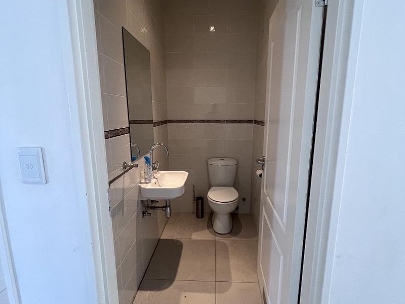 A compact, clean guest bathroom featuring a wall-mounted basin, toilet, and neutral floor-to-ceiling tiling.