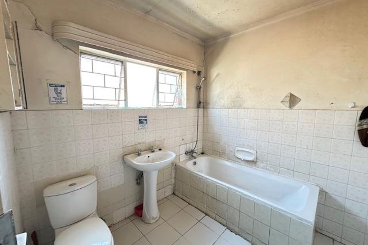 A dated bathroom featuring a standard bathtub, pedestal sink, and toilet, requiring significant renovation and cosmetic repairs to the walls and ceiling.
