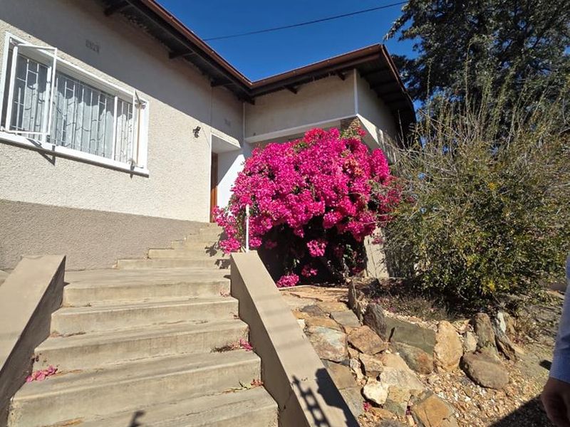 Front entrance of the house featuring a concrete staircase leading to the main door, complemented by a rockery garden and established bougainvillea.