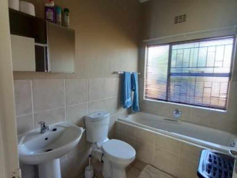 A functional bathroom featuring a pedestal basin, toilet, and bathtub with tiled splashbacks and tiled flooring.