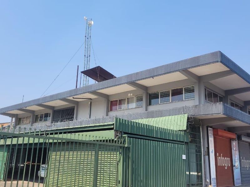 Exterior view of a commercial building featuring a concrete facade, metal roller shutter doors, and perimeter security fencing with razor wire.