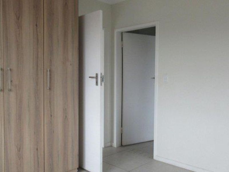 A clean, empty bedroom featuring neutral tiled flooring and modern wood-finish built-in cupboards.