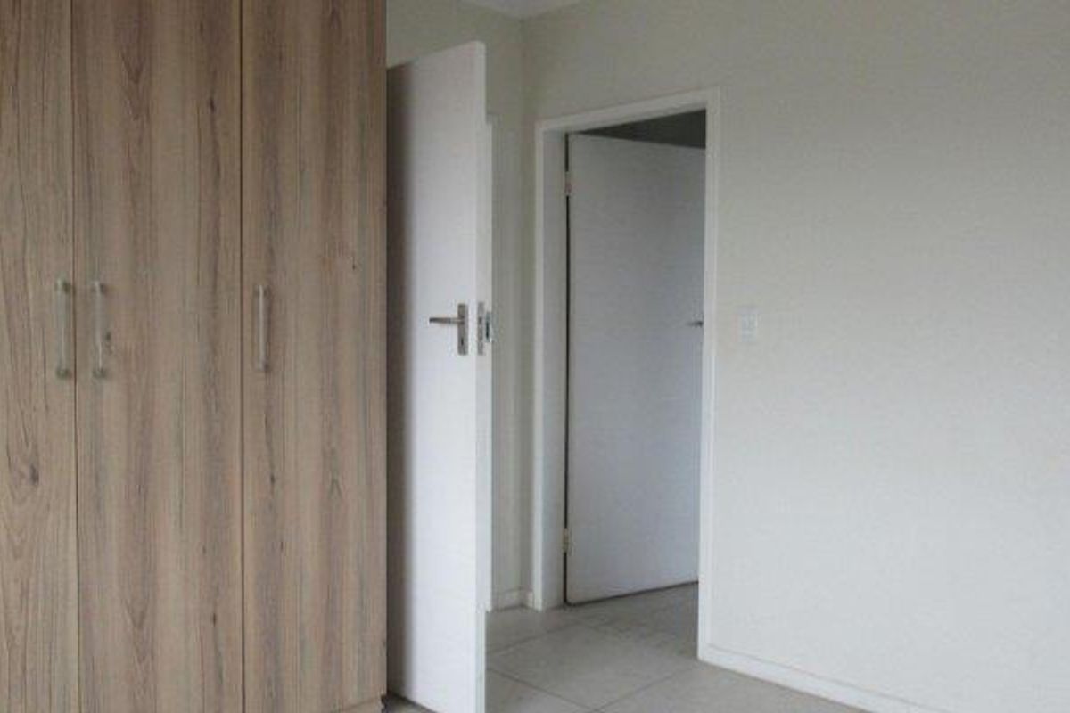 A clean, empty bedroom featuring neutral tiled flooring and modern wood-finish built-in cupboards.