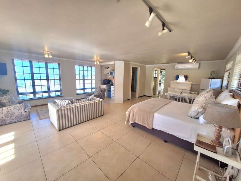 Spacious open-plan studio apartment featuring tiled flooring, track lighting, a split-system air conditioner, and a compact kitchenette area.