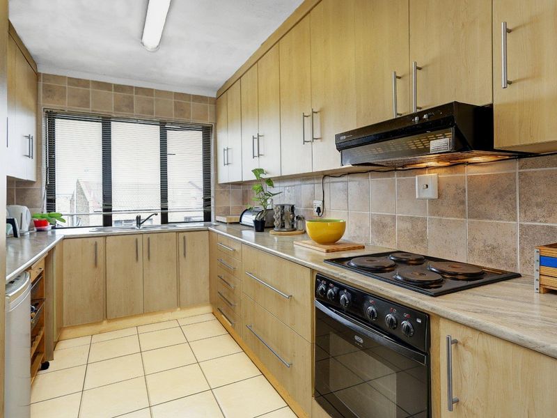 Functional kitchen featuring light wood-finish cabinetry, tiled backsplash, ceramic flooring, and integrated electric stove with extractor fan.