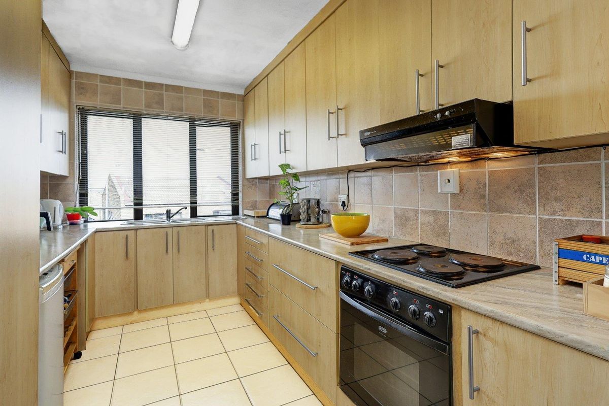 Functional kitchen featuring light wood-finish cabinetry, tiled backsplash, ceramic flooring, and integrated electric stove with extractor fan.