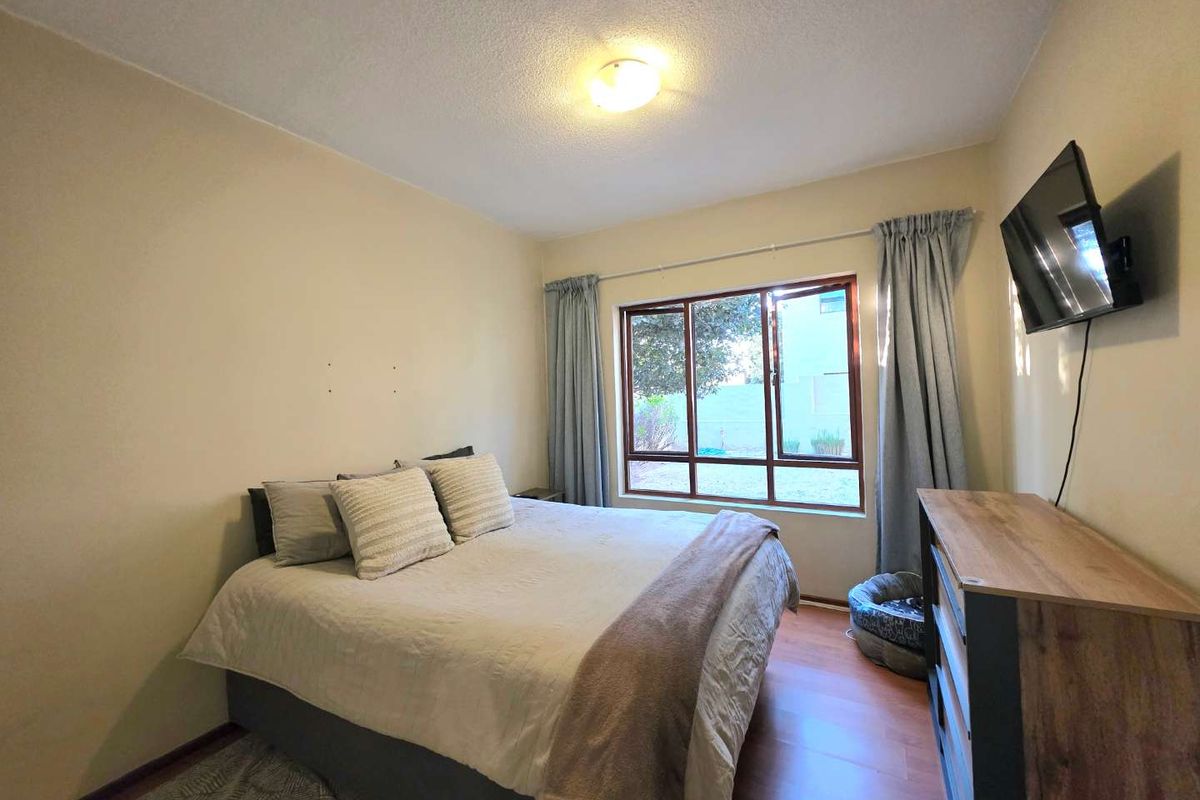 A functional bedroom featuring laminate flooring, a large window providing natural light, and a neutral wall finish.
