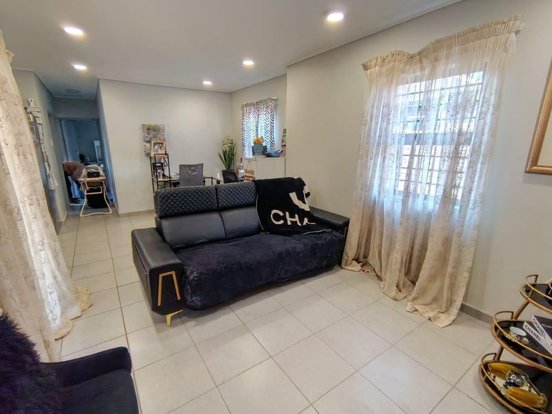A well-lit living room featuring neutral tiled flooring, recessed ceiling lighting, and window security bars, providing a functional and comfortable living space.