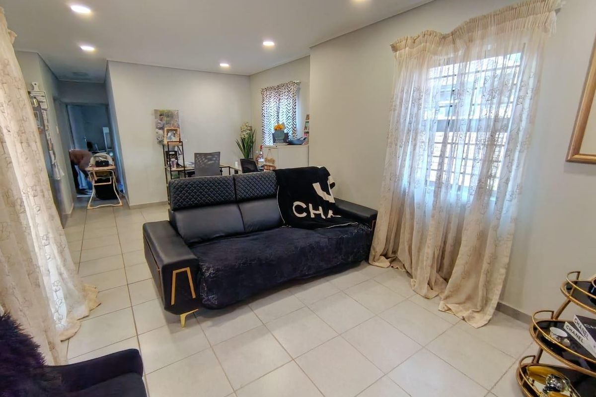 A well-lit living room featuring neutral tiled flooring, recessed ceiling lighting, and window security bars, providing a functional and comfortable living space.