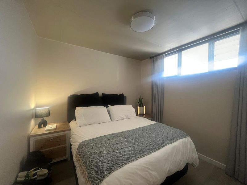 A functional bedroom featuring a horizontal sliding window with curtain tracks and a central ceiling light fixture.