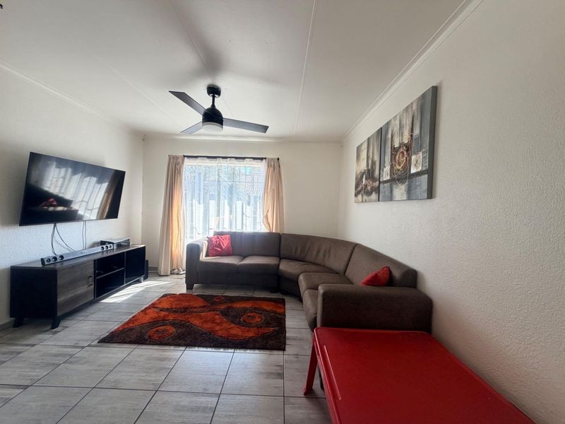 A functional living room featuring tiled flooring and a ceiling fan, providing a neutral base for potential interior updates.