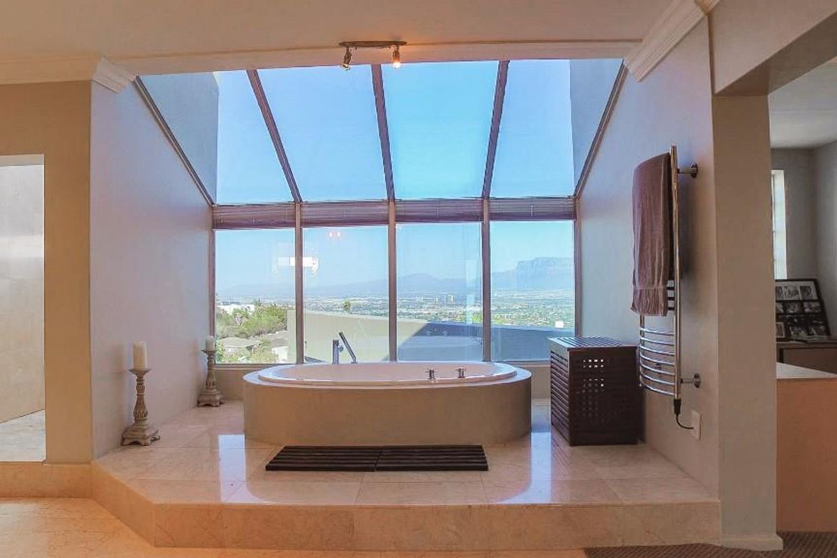 A luxurious bathroom featuring a raised built-in bathtub set against a large glass conservatory-style window with panoramic mountain and city views.