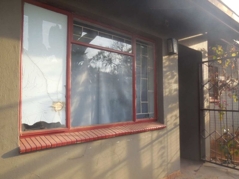 Front exterior view showing a metal security gate, external wall lighting, and a damaged window with a broken pane and brick sill.