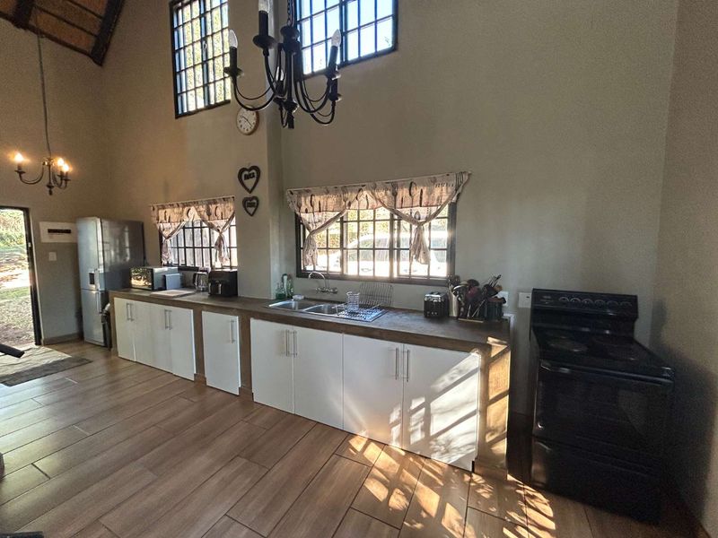 Spacious kitchen featuring white cabinetry, a double sink, tiled flooring, and a vaulted ceiling with natural light through lattice windows.