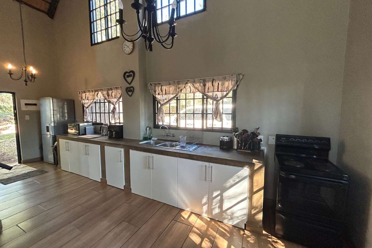Spacious kitchen featuring white cabinetry, a double sink, tiled flooring, and a vaulted ceiling with natural light through lattice windows.
