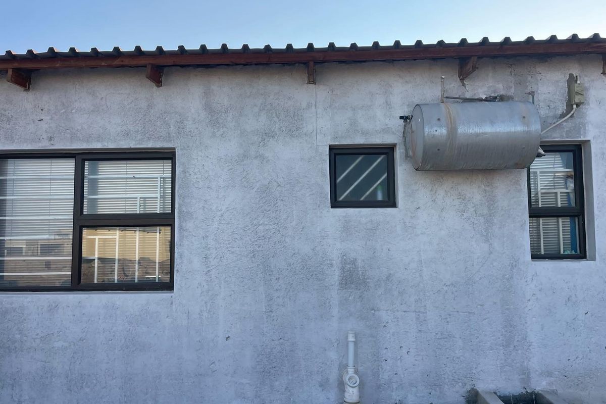 Exterior view of the property wall featuring aluminium window frames, an external geyser unit, and exposed roof rafters.