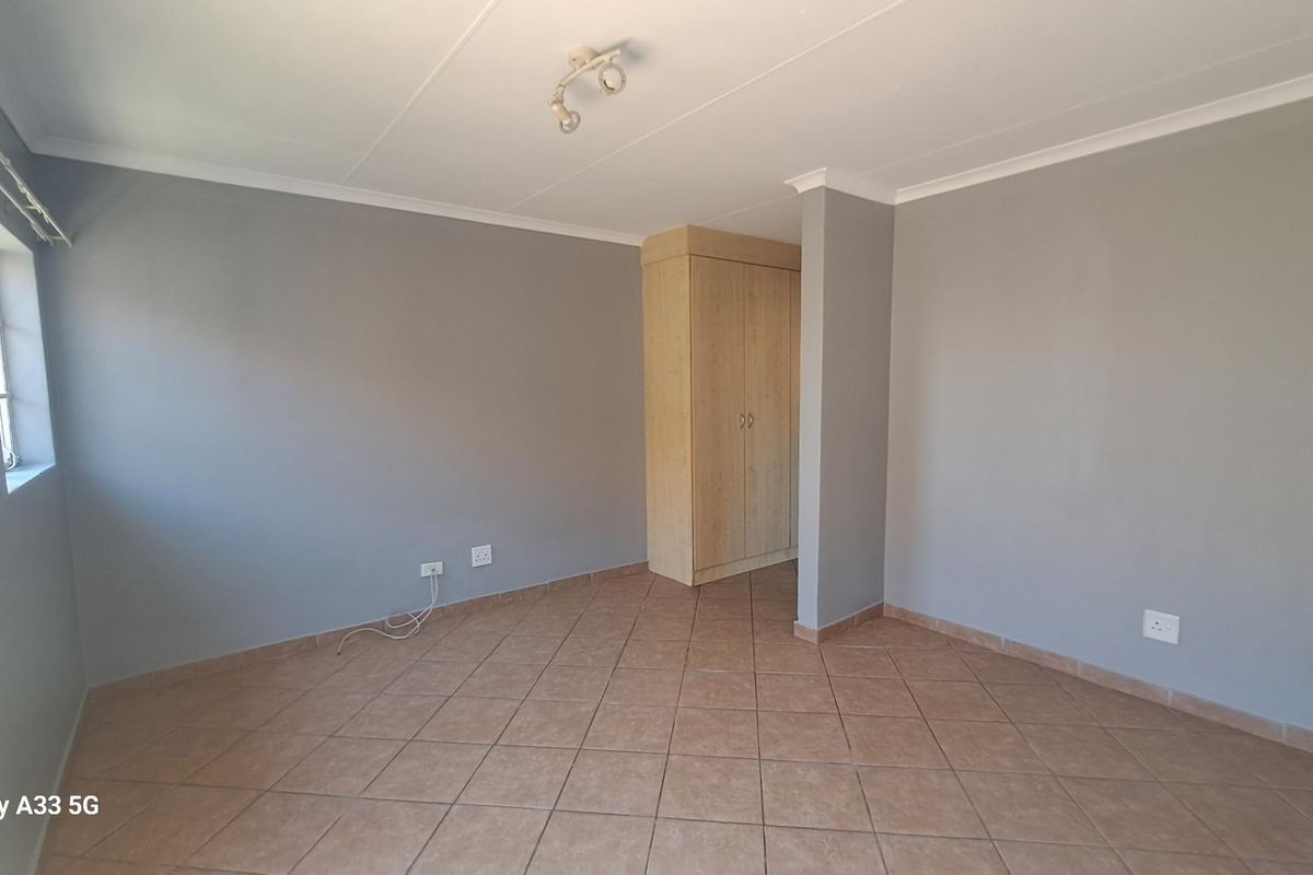 A clean, empty bedroom featuring neutral grey walls, tiled flooring, and a built-in wooden wardrobe.