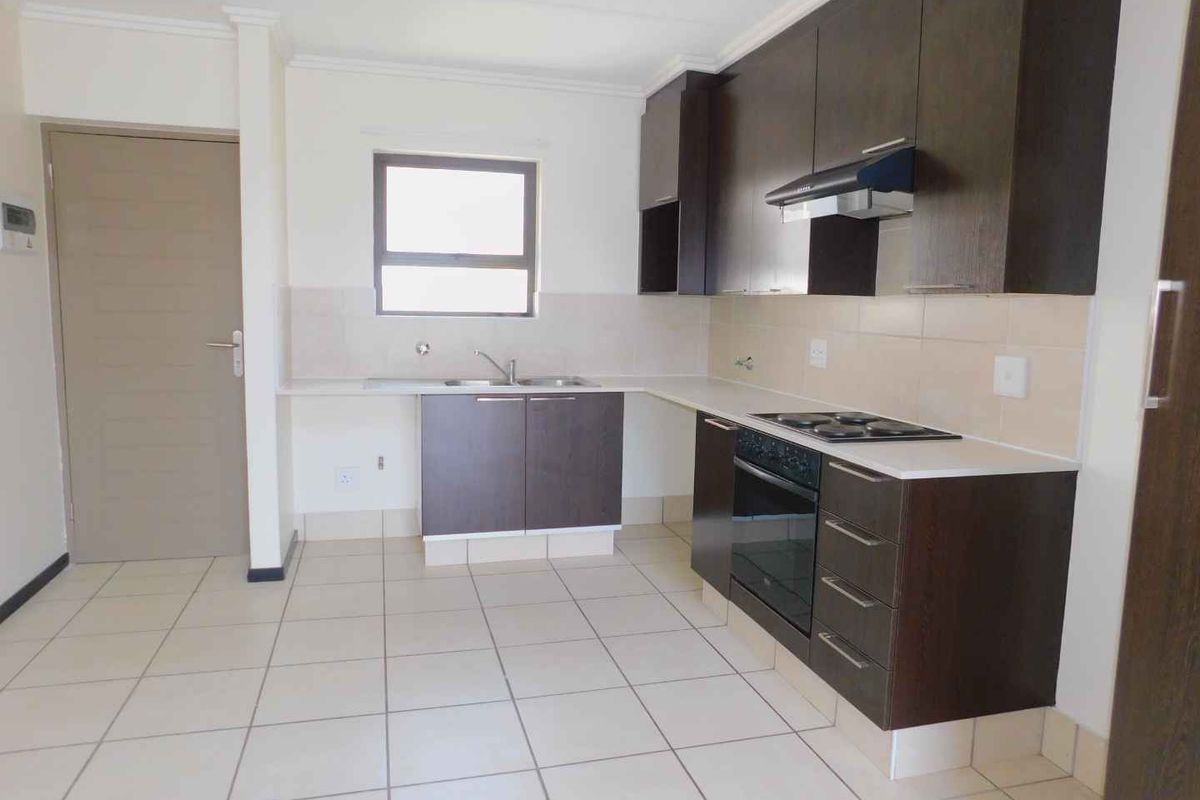 A clean, modern kitchen featuring dark wood cabinetry, built-in oven, electric hob, extractor fan, and tiled flooring in an open-plan layout.