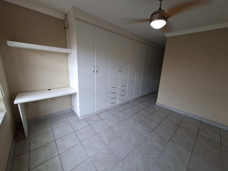 A spacious bedroom featuring extensive built-in cupboards, a integrated desk area, tiled flooring, and a ceiling fan.