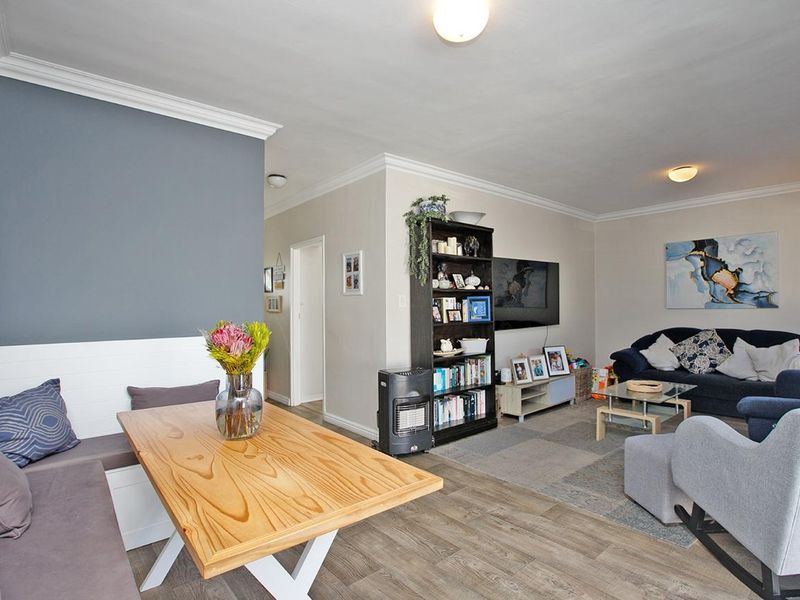 An open-plan living and dining area featuring laminate flooring, crown molding, and a built-in dining bench, creating a functional and cohesive living space.