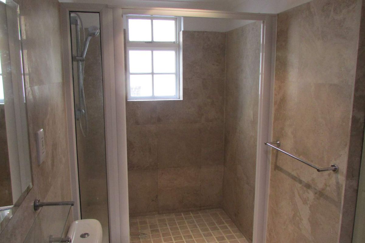 A functional bathroom featuring a walk-in shower with glass enclosure, tiled walls, and a window for natural light.