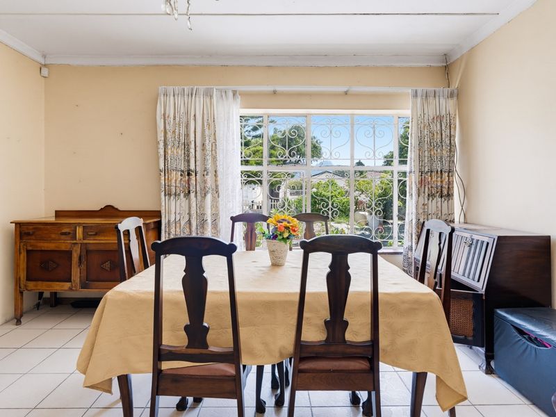 A dining room featuring tiled flooring, a large window with security bars, and coved ceiling detailing, offering a functional space for family meals.