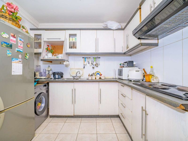 A functional kitchen featuring white cabinetry, laminate countertops, tiled backsplash, and integrated electric hob with extractor fan.