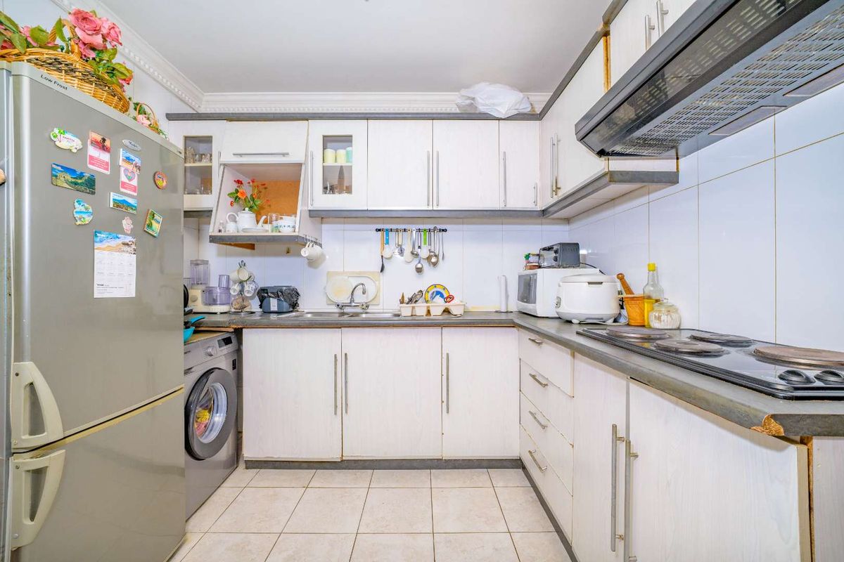 A functional kitchen featuring white cabinetry, laminate countertops, tiled backsplash, and integrated electric hob with extractor fan.