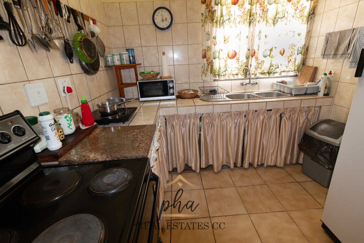 A compact kitchen featuring tiled countertops, a double basin sink, and a freestanding electric stove with a tiled backsplash.