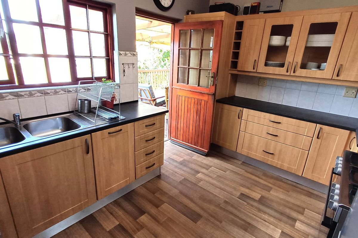 A functional kitchen featuring light wood cabinetry, dark countertops, a double stainless steel sink, and direct access to an outdoor patio area.