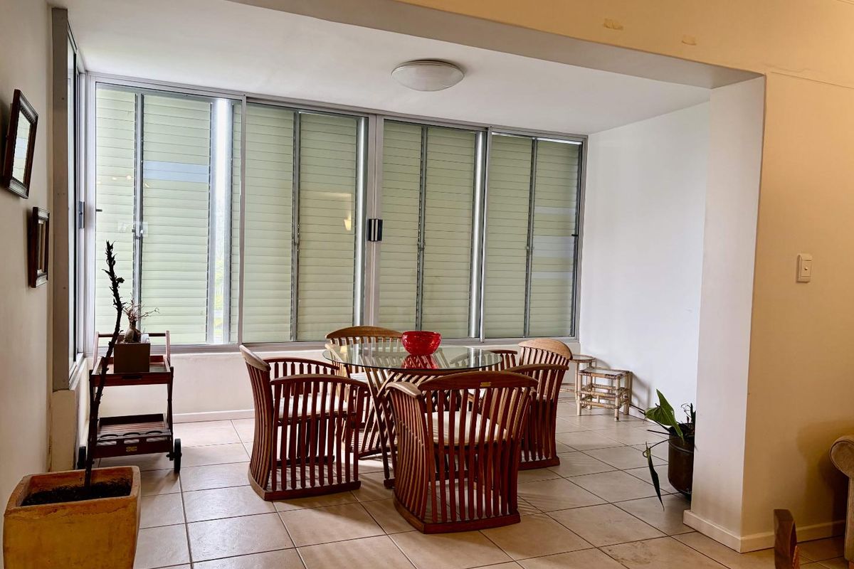 A sunlit living area featuring large sliding windows and neutral tiled flooring, offering a versatile space for dining or relaxation.