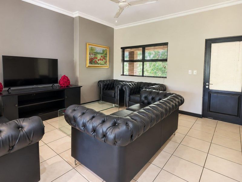 A well-maintained living room featuring neutral walls, tiled flooring, a ceiling fan, and a dark-framed door leading to an exterior space.