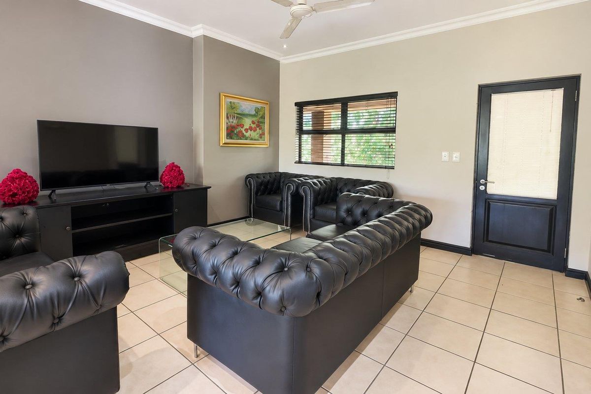 A well-maintained living room featuring neutral walls, tiled flooring, a ceiling fan, and a dark-framed door leading to an exterior space.