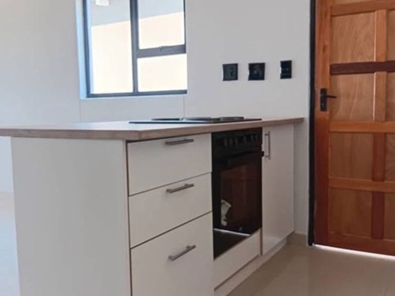 A clean, modern kitchen island featuring built-in oven, hob, and cabinetry, set against a neutral interior with tiled flooring and a timber door.