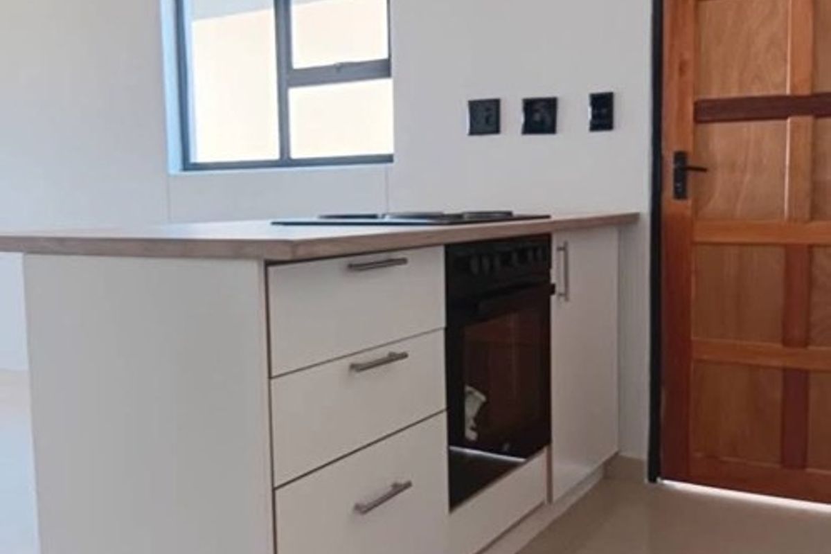 A clean, modern kitchen island featuring built-in oven, hob, and cabinetry, set against a neutral interior with tiled flooring and a timber door.