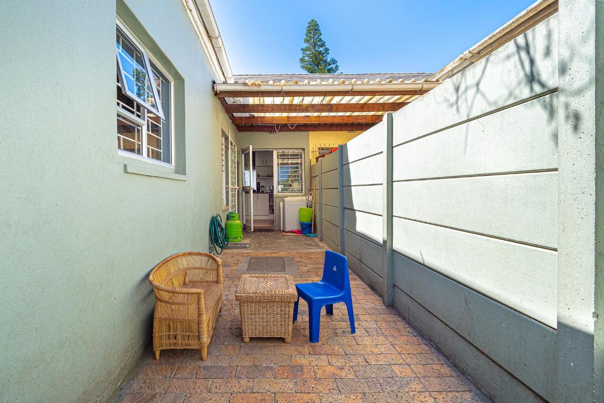 A private rear courtyard featuring paved flooring, a precast concrete boundary wall, and a timber pergola structure providing partial shade.