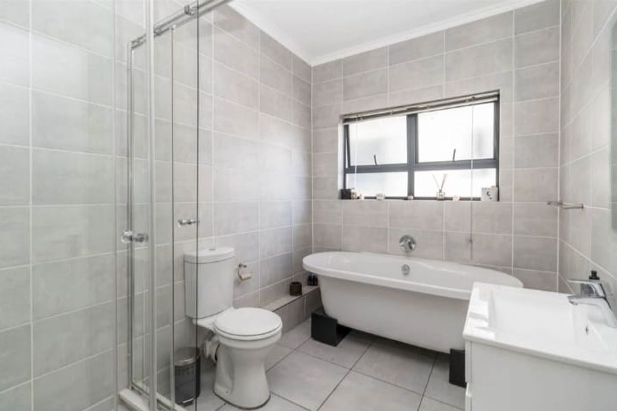 Modern bathroom featuring a freestanding bathtub, separate glass-enclosed shower, vanity basin, and neutral floor-to-ceiling ceramic tiling.